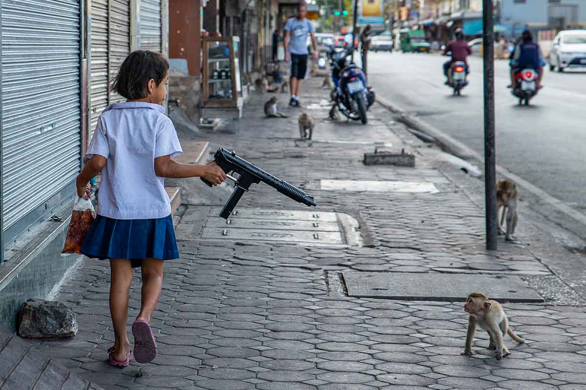 meisje op straat richt een geweer naar een aap - joan de la malla - nature talks photo festival Vogelfotografie in Afrika gemaakt door fotograaf Herman van der Hart